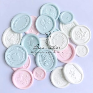 May include: A collection of pastel-colored wax seals in shades of blue, pink, and white. The seals feature various embossed designs, including flowers, swans, butterflies, and ornate frames. The text "Bea's Atelier Handmade-Made in Italy" is also visible.