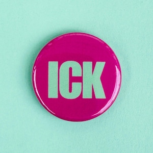Puede incluir: Un botón redondo magenta con la palabra "ICK" en letras mayúsculas verde claro. El botón tiene un acabado brillante y está sobre un fondo verde azulado claro. Este botón es un accesorio divertido.