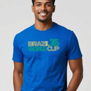 May include: A blue t-shirt with the words "BRAZIL 26 WORLD CUP" in yellow, green, and white. The shirt has short sleeves and a crew neck. The text is in a bold, stylized font.