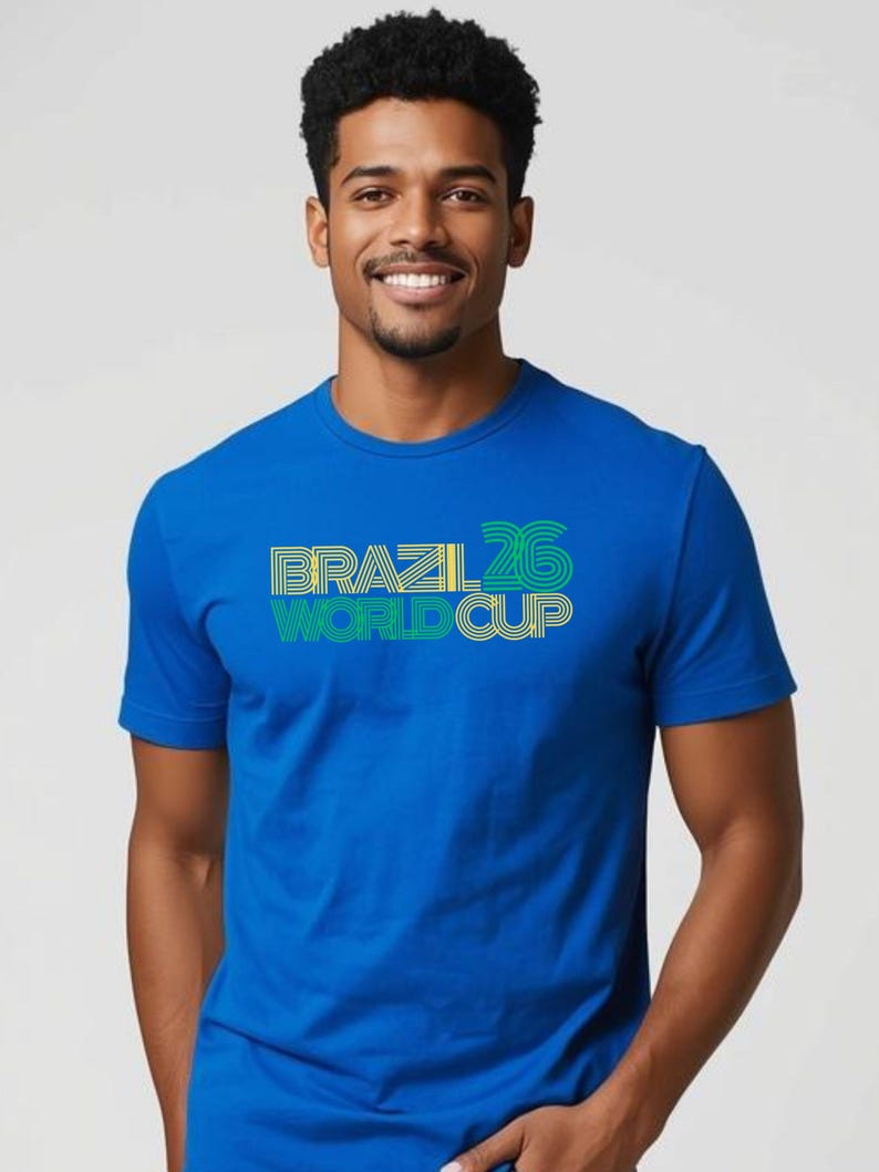 May include: A blue t-shirt with the words "BRAZIL 26 WORLD CUP" in yellow, green, and white. The shirt has short sleeves and a crew neck. The text is in a bold, stylized font.