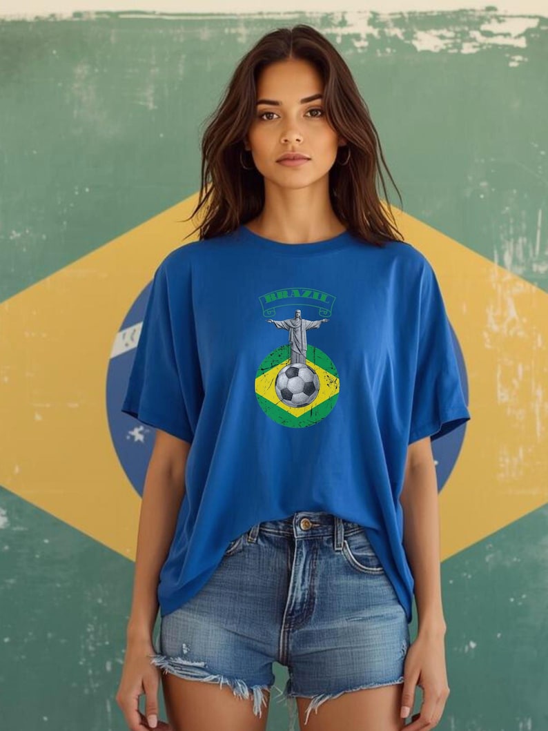 May include: A blue t-shirt featuring a graphic of Christ the Redeemer, a soccer ball, and the word "BRAZIL" in green. The shirt is paired with denim shorts. The background is a Brazilian flag.