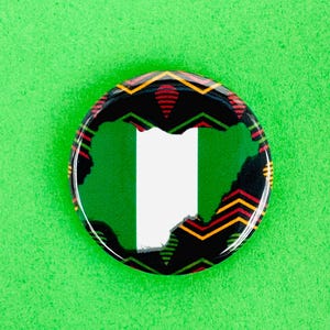 Peut inclure: Un bouton rond et brillant, représentant la carte du Nigeria en vert et blanc. Le bord du bouton est noir avec un motif géométrique coloré rouge, jaune et vert. Sur un fond vert vif.