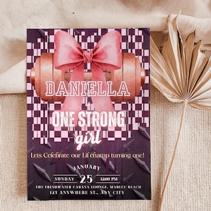 May include: A rectangular invitation card featuring a pink bow over a brown dumbbell, set against a pink and dark purple checkered background. Text reads: DANIELLA is ONE STRONG girl, Lets Celebrate our Lil champ turning one! JANUARY SUNDAY 25 12:00 PM, THE FRESHWATER CABANA LOUNGE, MARLEY BEACH, 123 ANYWHERE ST., ANY CITY.
