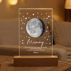 May include: A lighted acrylic panel with a full moon illustration and star accents. The panel reads "Mummy" with a personalized message and sits on a wooden base. The lamp is a decorative home accent.