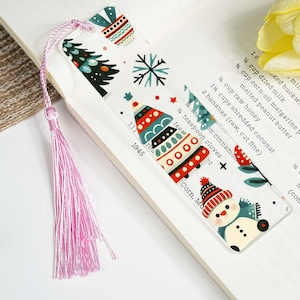 Op de afbeelding: Een kerstthema bladwijzer met een roze kwast. De bladwijzer toont feestelijke illustraties van een kerstboom, sneeuwpop en ornamenten in rood, groen en wit. De tekst "1945" is ook zichtbaar.