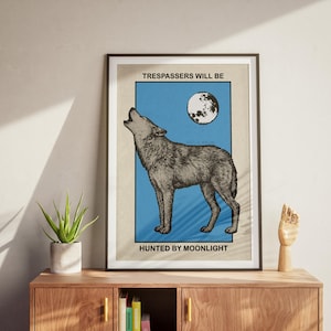 May include: A framed wall art print featuring a detailed illustration of a wolf howling at a full moon against a blue background. The text "TRESPASSERS WILL BE" appears above the wolf, and "HUNTED BY MOONLIGHT" is printed below the illustration.
