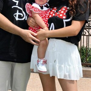 May include: A black t-shirt with a white Disney logo, a black t-shirt with a red and white polka dot Minnie Mouse bow graphic, a red and white polka dot dress with a Minnie Mouse collar, a white tiered skirt, and white sneakers with red bows.
