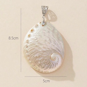 May include: An oval pendant, 8.5 cm long and 5 cm wide, with a pearlescent finish. It features a silver-coloured bail and a small, clear crystal. The pendant has a natural, iridescent sheen and a textured surface, resembling a seashell.