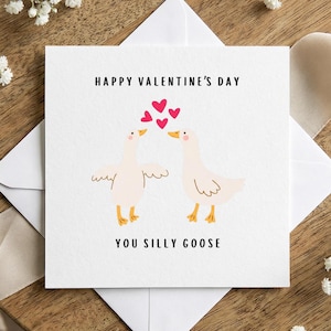 Puede incluir: Una tarjeta blanca de San Valentín con el texto "Happy Valentine's Day" y "You Silly Goose". La tarjeta presenta dos gansos de dibujos animados con corazones sobre sus cabezas. La tarjeta está en un sobre blanco.