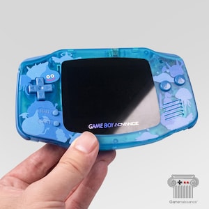 May include: A blue Game Boy Advance handheld console with a transparent shell. The shell features a sea creature design in shades of blue. The screen is black, and the text "GAME BOY ADVANCE" is visible.