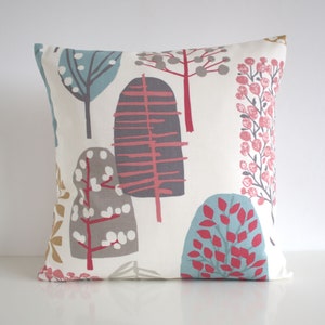 May include: A square throw pillow with an off-white background featuring a repeating pattern of stylized trees in shades of blue, gray, pink, and mustard yellow. The design includes various tree shapes with leaf and branch details.