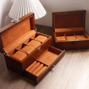 May include: Two wooden watch boxes with orange velvet interiors. One box has a pull-out drawer for rings. The boxes are open, revealing compartments for watches and other jewellery. The wood has a rich, dark brown finish.