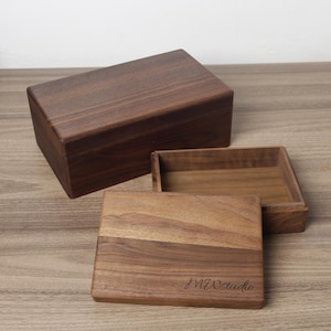 May include: A rectangular dark brown wooden box with a lid, accompanied by a separate open wooden tray. The lid features the engraved text MWstudio in a cursive script. The wood grain is visible across the surfaces of both the box and the tray.