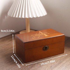 May include: A brown wooden box with a lock and an initial design on the lid. The box measures 19cm long, 11cm high, and 9cm deep. The box has a vintage aesthetic.