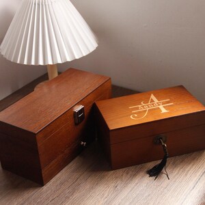 May include: Two rectangular wooden boxes in a dark brown finish. One box has a metal clasp, the other is engraved with the name "Aandy". The boxes are likely for storage or display, and are placed on a wooden surface.