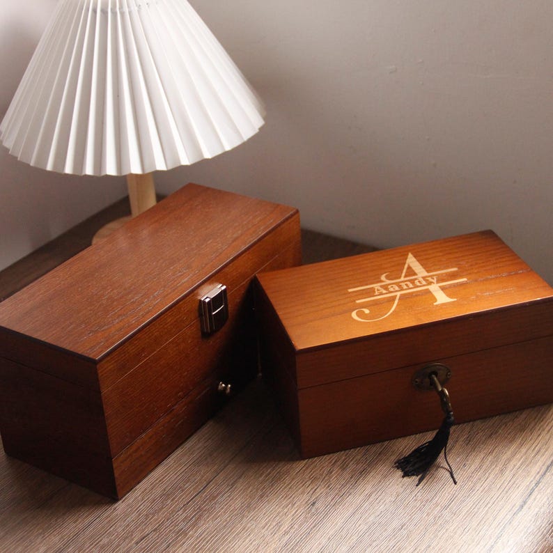 May include: Two rectangular wooden boxes in a dark brown finish. One box has a metal clasp, the other is engraved with the name "Aandy". The boxes are likely for storage or display, and are placed on a wooden surface.