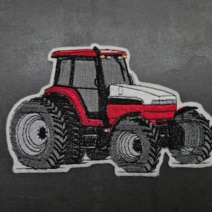 Könnte beinhalten: Gestickter Aufnäher mit einem roten, weißen und schwarzen Traktor. Der Traktor hat große, detaillierte Reifen und eine graue Kabine. Der Aufnäher ist weiß umrandet.