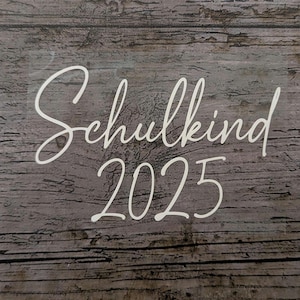 May include: White script text on a wooden background reads "Schulkind 2025." The text is in a cursive font, with the year in a simple, clean font. The background has a rustic, weathered wood grain.