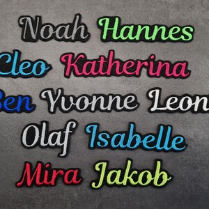 Könnte beinhalten: Gestickte Namensaufnäher in verschiedenen Farben, darunter Grün, Blau, Pink und Rot. Namen sind Noah, Hannes, Cleo, Katherina, Ben, Yvonne, Leonie, Olaf, Isabelle, Mira und Jakob. Die Aufnäher haben einen schwarzen Rand.