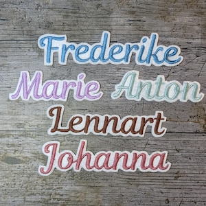 May include: Embroidered name patches in various colors, including blue, purple, teal, brown, and pink, are displayed on a wooden surface. The names Frederike, Marie, Anton, Lennart, and Johanna are featured in a cursive font.