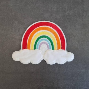 Könnte beinhalten: Ein farbenfroher Regenbogen-Aufnäher mit rotem Rand, der Bänder in Orange, Gelb, Grün, Blau und Lila zeigt. Zwei weiße Wolkenformen befinden sich darunter. Geeignet für Kleidung oder Accessoires.