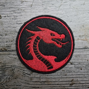 Könnte beinhalten: Runder, gestickter Aufnäher mit einem roten Drachen-Design auf schwarzem Hintergrund. Der Drache ist mit offenem Maul und langem Hals dargestellt. Geeignet für Kleidung oder Accessoires.