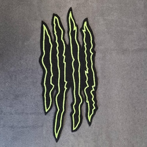 Könnte beinhalten: Schwarzer, gestickter Aufnäher mit einem Krallenabdruck-Design und neongrünen Umrissen. Die Krallenmarkierungen sind vertikal und gezackt, was einen auffälligen Kontrast erzeugt. Geeignet für Jacken, Taschen oder andere Kleidungsstücke.