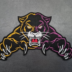 Könnte beinhalten: Ein schwarzer, gestickter Panther-Aufnäher mit gelben und lila Akzenten. Der Panther knurrt, mit weißen Zähnen und Krallen. Der Aufnäher ist ein stilisiertes Design, geeignet für Jacken, Taschen oder andere Kleidungsstücke.