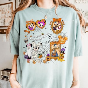 Puede incluir: Camiseta azul claro con un diseño de Halloween de Disney. El diseño incluye Mickey y Minnie Mouse, el Pato Donald y Goofy con disfraces de Halloween, rodeados de telarañas, calabazas y el texto "Disney Halloween Day".