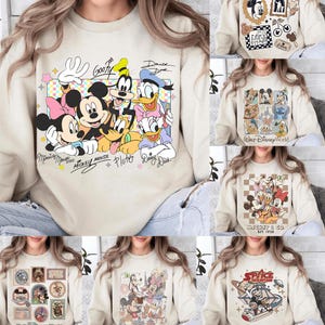 May include: Beige sweatshirts with Disney character designs. One features Mickey Mouse, Minnie Mouse, Donald Duck, Daisy Duck, Goofy, and Pluto. Other designs include Mickey & Co., Space Mountain, and various Disney World graphics.
