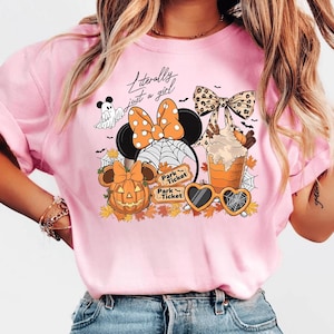May include: Pink t-shirt with a Halloween-themed graphic. The design includes a Minnie Mouse silhouette with an orange polka dot bow, a pumpkin, a ghost, and the text "Literally just a girl". The shirt also features a spider web and fall leaves.