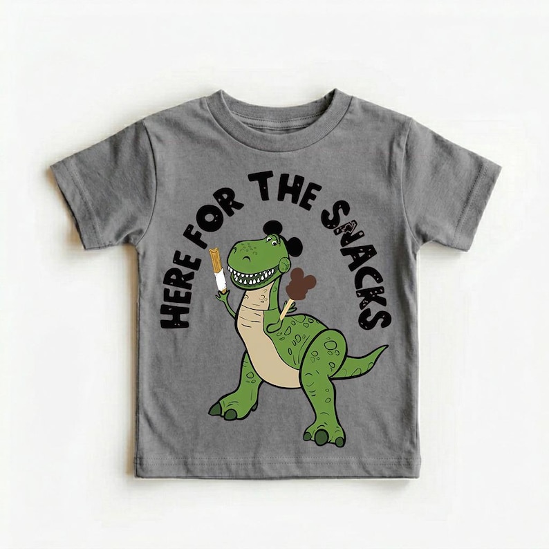 May include: Gray short-sleeved t-shirt featuring a green cartoon dinosaur holding ice cream treats. The text "HERE FOR THE SNACKS" arches above the dinosaur. The dinosaur has a light tan belly and black mouse ears.