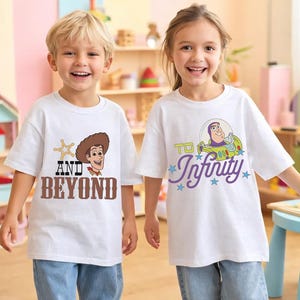 Puede incluir: Dos niños con camisetas blancas con diseños de personajes de dibujos animados. Una camiseta dice "AND BEYOND" con un gráfico de Woody. La otra dice "TO Infinity" con un gráfico de Buzz Lightyear. Ambos niños sonríen.