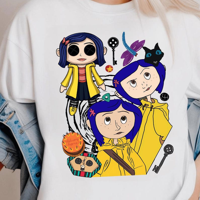 May include: White t-shirt featuring a cartoon illustration of a character with blue hair and a yellow coat. The design includes a black cat, keys, and the text "Welcome Home" on a cake.