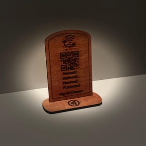 Könnte beinhalten: Ein hölzernes WLAN-Schild mit abgerundeter Oberseite und rechteckiger Basis. Das Schild hat einen QR-Code und den Text "Network, Password, Tap To Connect". Das Schild ist braun und hat oben ein tropisches Design.