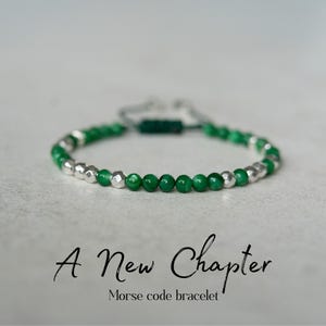 May include: A green and silver beaded bracelet with the text "A New Chapter" and "Morse code bracelet". The bracelet features alternating green and silver beads, with a sliding knot closure.