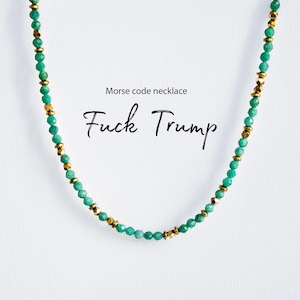 May include: A beaded necklace with green and gold accents. The necklace features small, round green beads interspersed with gold-colored spacers. The text "Morse code necklace" and "Fuck Trump" are displayed in black script.