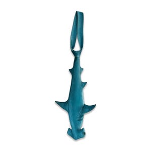 May include: A teal-coloured necktie shaped like a hammerhead shark. The tie features a smooth, matte finish with a distinct hammer-shaped head at the bottom, side fins, and a long, tapered body that extends upwards into a knotted loop for wearing.
