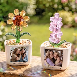 May include: Two white square ceramic planters containing glass flowers and small pebbles. The left planter features a yellow glass sunflower and a photo with the text "Best Friend". The right planter has a pink glass flower and a photo with the text "soul sister forever".