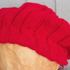 May include: A red knitted beret with a cable knit pattern.
