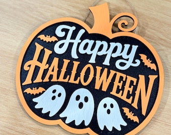 Puede incluir: Decoración de Halloween de madera con forma de calabaza. El diseño presenta las palabras "Happy Halloween" en blanco y naranja, junto con fantasmas blancos y murciélagos naranjas. La decoración está diseñada para colgarse.