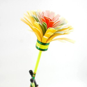 May include: A handmade paper flower with a yellow stem and a multi-colored flower head. The flower head features layers of yellow, green, orange, pink, and white paper. The stem is light green with green and yellow stripes near the base.