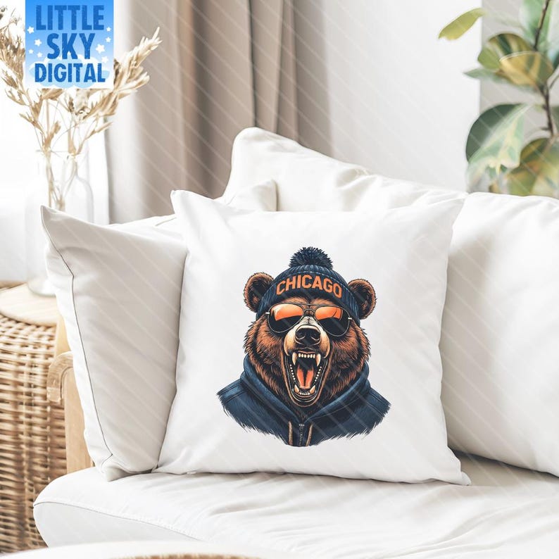 Decorative pillow on a white couch featuring a graphic of a roaring bear wearing a dark hoodie, orange sunglasses, and a navy beanie with “CHICAGO” in orange text. The living room setting includes a wicker side table with a vase of dried flowers and a leafy green plant, creating a warm, cozy atmosphere ideal for showcasing home decor or sports-themed merchandise.