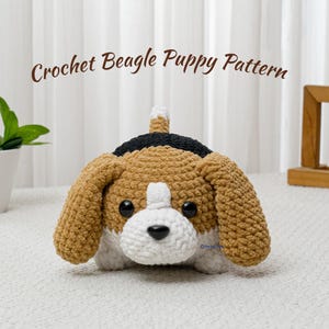 Pode incluir: Um cachorrinho beagle de crochê em bege, branco e preto. O cachorrinho tem orelhas grandes e caídas, um nariz preto e uma cauda pequena. O texto "Crochet Beagle Puppy Pattern" está acima do cachorrinho.