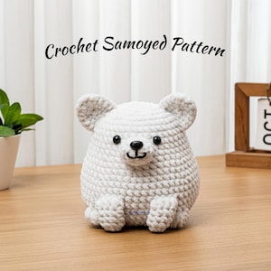May include: A handmade, white crochet bear with black eyes and a stitched nose and mouth. The bear is sitting on a wooden surface. The text "Crochet Samoyed Pattern" is above the bear.