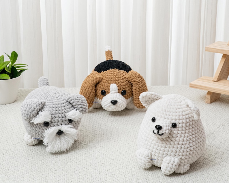 May include: Three handmade crochet dog toys. A gray Schnauzer with a white beard, a brown and white Beagle, and a white dog with black eyes and nose. The toys are on a white surface.
