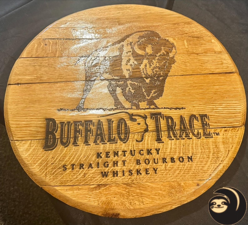 May include: A circular wooden sign featuring the words "Buffalo Trace" and a bison image. The sign also includes the text "Kentucky Straight Bourbon Whiskey". The wood has a natural, light brown colour.