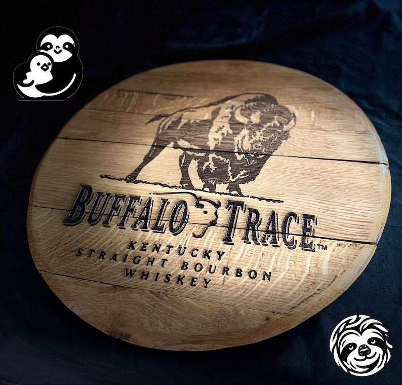 May include: A circular wooden sign displaying the Buffalo Trace logo and text. The sign features a detailed image of a bison and the words "Buffalo Trace Kentucky Straight Bourbon Whiskey". The wood has a natural grain and a warm, brown colour.