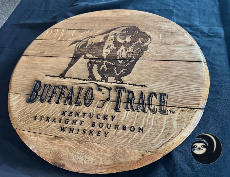 May include: Circular wooden sign featuring the text "Buffalo Trace Kentucky Straight Bourbon Whiskey" and a bison illustration. The sign is made of light brown wood with dark brown text and image.
