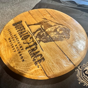 May include: Circular wooden lid from a Buffalo Trace whiskey barrel. The lid is made of light brown wood and features the brand name and a bison illustration. The text reads "Straight Kentucky Bourbon Whiskey."